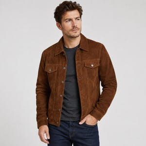 May include: A brown suede jacket featuring a classic collar, long sleeves, and a front button closure. The jacket includes two chest pockets with buttoned flaps and metallic buttons down the center placket, worn over a dark gray t-shirt and blue jeans.