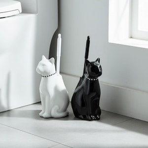 May include: Two ceramic cat-shaped toilet brush holders, one white and one black. Each has a decorative collar and a brush. The holders are designed to sit on the floor, adding a touch of whimsy to the bathroom.