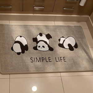 May include: Rectangular gray floor mat with three panda bear illustrations in black and white. The text "SIMPLE LIFE" is printed in black below the pandas. The mat has a gray border.