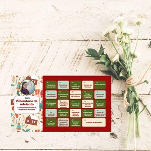 Könnte beinhalten: Ein Adventskalender mit täglichen Aktivitäten wie Filmabenden und DIY-Bastelarbeiten. Der rot-grüne Kalender mit einem Foto einer Person liegt auf einer weißen Holzoberfläche mit einem Blumenstrauß.