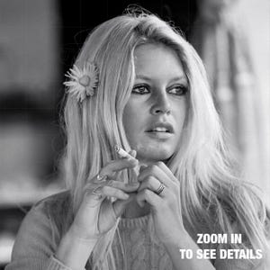 A black and white portrait of a woman with long blonde hair, holding a cigarette in her hand and looking off to the side.