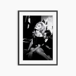 A black and white photograph of a woman sitting on a chair, with a man sitting next to her.