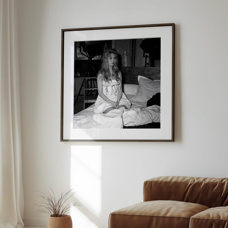 A framed black and white photograph of a woman sitting on a bed in a living room.