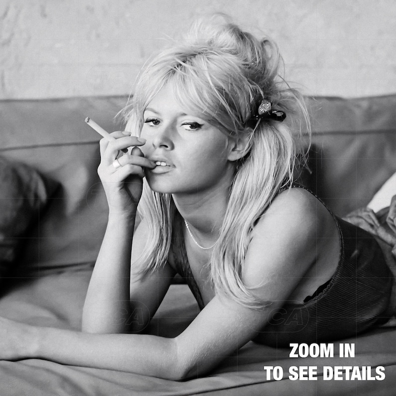 A black and white image of a woman lying on a couch, smoking a cigarette and looking directly at the camera.