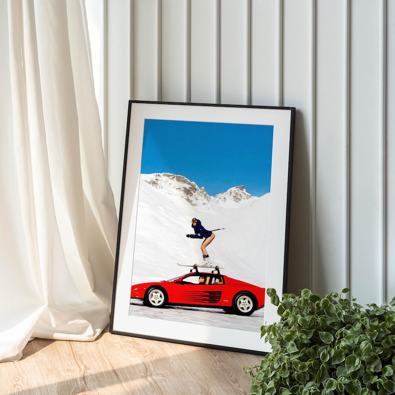 A framed photograph of a person skiing on a snowy mountain, with a red sports car parked nearby.