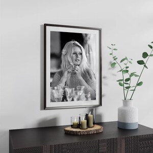 a framed black and white photograph of a woman with blonde hair, hanging on a wall above a wooden table with a vase of greenery and candles on it.