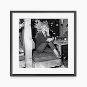 A black and white photograph of a woman sitting on a wooden bench, smiling and looking directly at the camera.