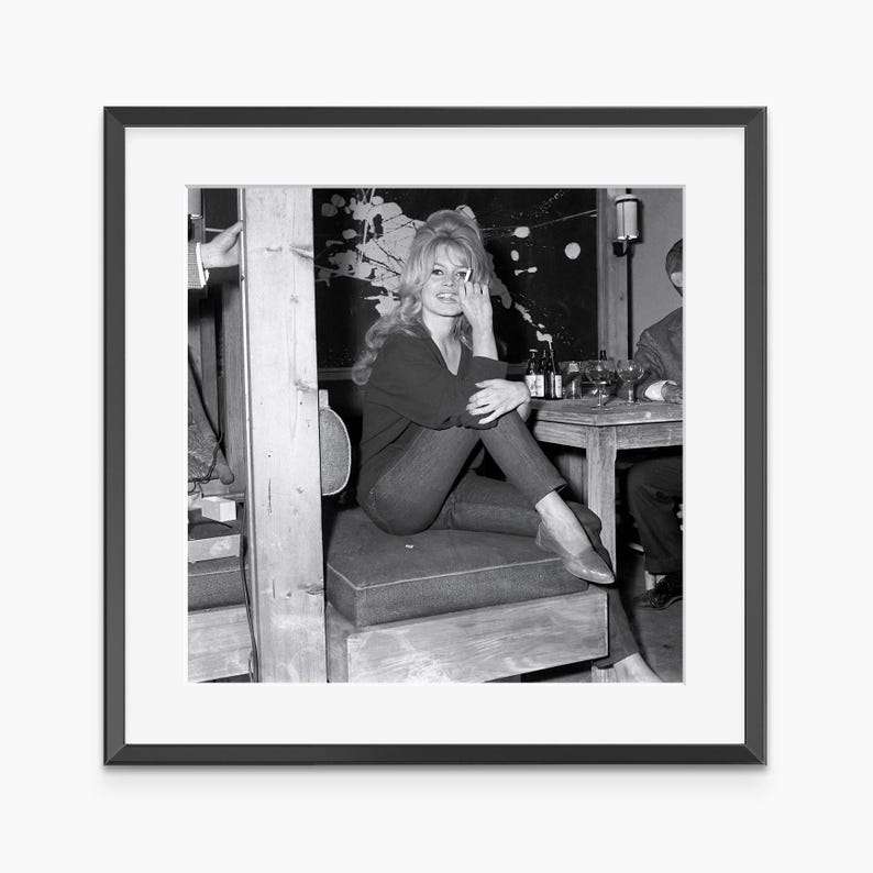 A black and white photograph of a woman sitting on a wooden bench, smiling and looking directly at the camera.
