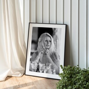 A framed black and white photograph of a woman with long blonde hair is displayed on a wooden surface, next to a potted plant.