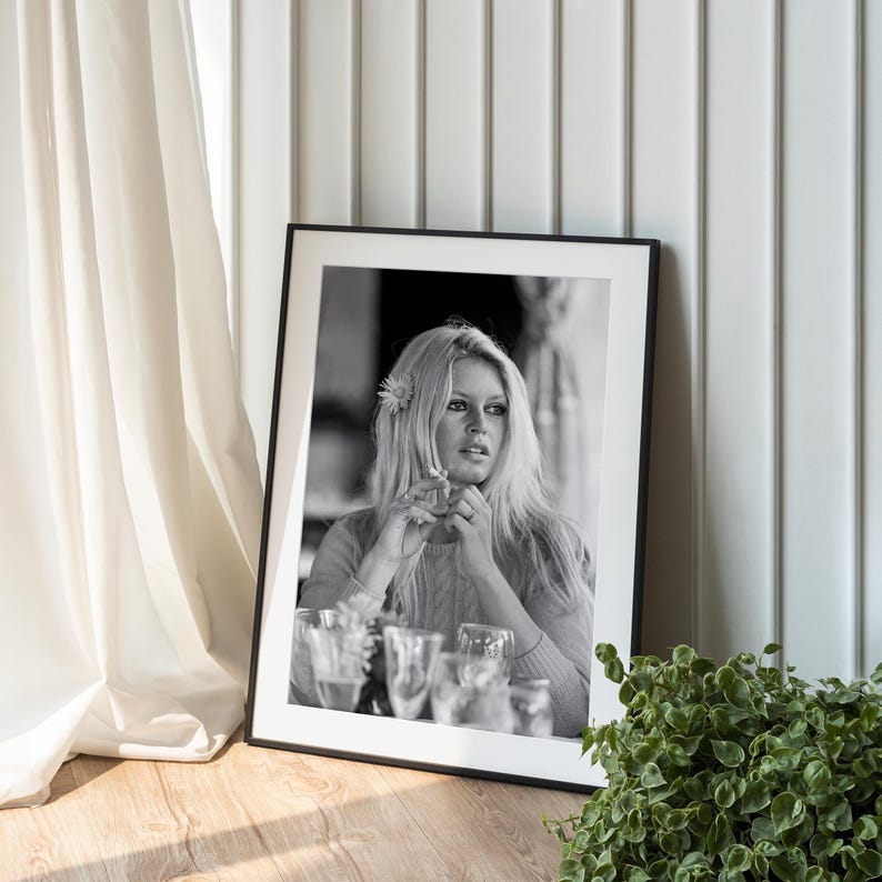 A framed black and white photograph of a woman with long blonde hair is displayed on a wooden surface, next to a potted plant.