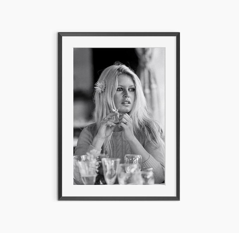 A black and white photograph of a woman sitting at a table, with wine glasses and a flower in her hair.
