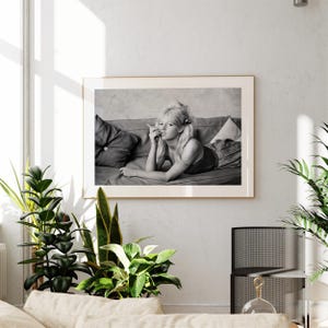 a framed black and white photograph of a woman lying on a couch, with a potted plant and a glass sculpture in the foreground.