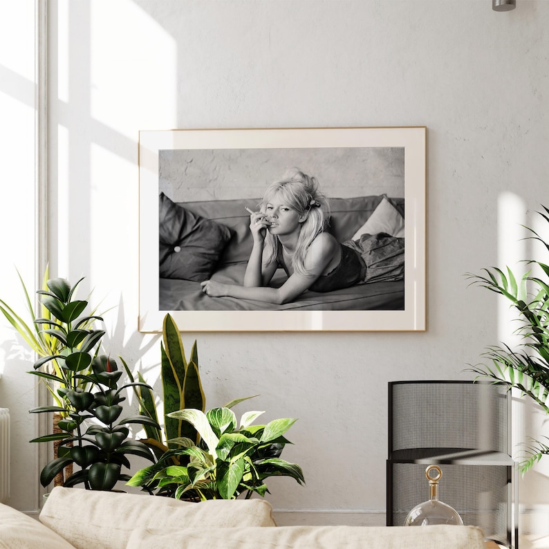 a framed black and white photograph of a woman lying on a couch, with a potted plant and a glass sculpture in the foreground.