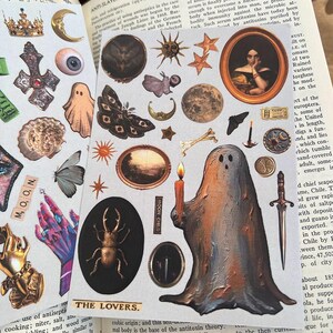 May include: A collection of vintage-style stickers featuring celestial and gothic imagery. Includes moons, stars, a ghost holding a candle, a portrait, insects, and the text "MOON" and "THE LOVERS."
