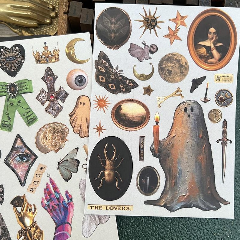 May include: Two sheets of decorative stickers featuring celestial and gothic designs. Includes moons, stars, butterflies, portraits, and a ghost holding a candle. Text includes "MOON CHILD" and "THE LOVERS."