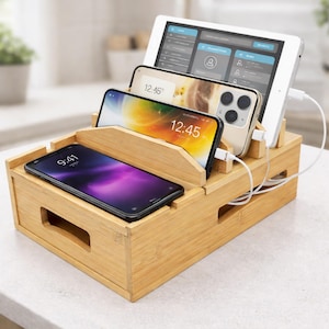 May include: A bamboo charging station holds a tablet and three smartphones. The devices are in different positions, with the tablet at the back and the phones in front. The screens display various apps and the time. White charging cables are connected to the devices.
