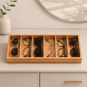 May include: A rectangular bamboo organizer tray with six individual vertical compartments. Each section holds a pair of eyeglasses or sunglasses, including frames in black, tortoiseshell, and thin gold metal, arranged in a single row.