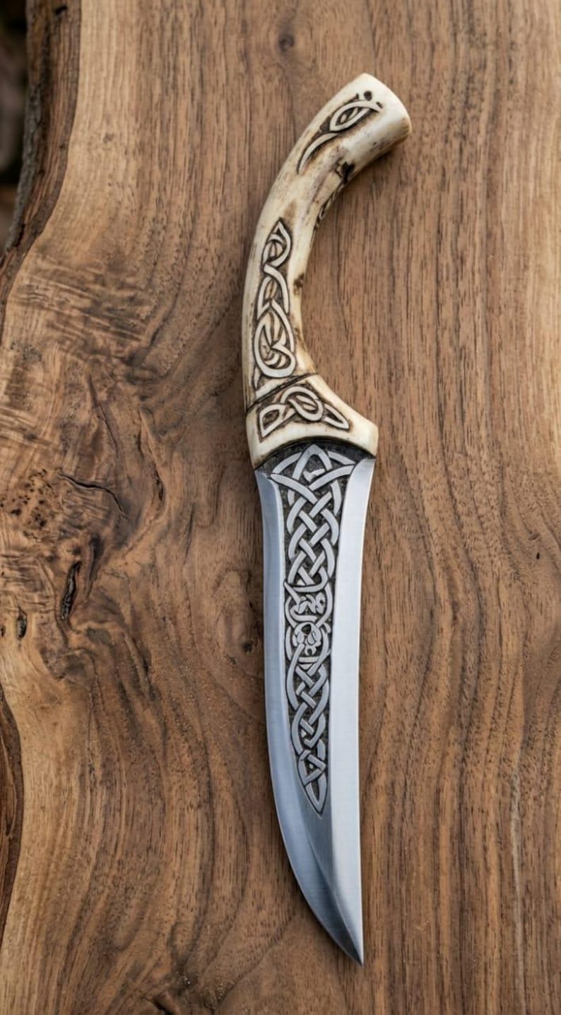 May include: A handcrafted knife with a bone handle and a stainless steel blade. The handle features intricate Celtic knotwork carvings. The blade has a curved shape and is set against a wooden background.