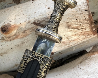 May include: An ornate sword with a detailed gold and silver handle and a clear, glass-like blade. The hilt features intricate patterns and designs. The sword's sheath is black with gold accents.