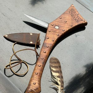 Puede incluir: Un cuchillo de madera hecho a mano con una hoja de acero inoxidable, remaches y una funda de cuero. El mango presenta tallas decorativas y está acompañado de una pluma. El cuchillo mide unos 25 cm de largo.