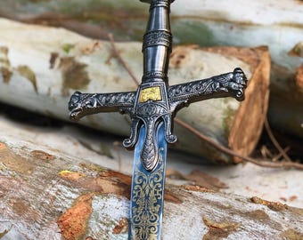 May include: A decorative sword with a silver and gold finish. The blade features an ornate gold pattern against a blue background. The hilt has a detailed design with a gold emblem.