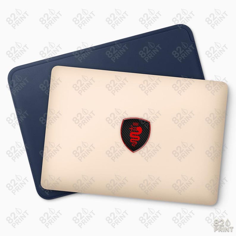 Pu&ograve; includere: Una custodia per laptop blu navy con una custodia per laptop beige chiaro sopra. La custodia per laptop presenta un emblema nero e rosso. L'emblema ha la forma di uno scudo con un disegno di serpente rosso.