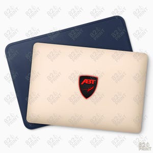 May include: A navy blue laptop sleeve with a light beige laptop sleeve on top. The light beige sleeve has a red and black ABT logo. The navy blue sleeve is slightly larger. The background is white.