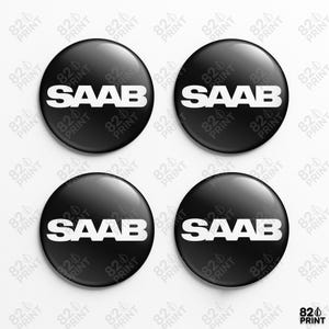 Könnte beinhalten: Vier schwarze, glänzende runde Knöpfe mit dem weißen Wort "SAAB" auf jedem. Die Knöpfe sind in einem quadratischen Muster auf weißem Hintergrund angeordnet. Wahrscheinlich Auto Zubehör.