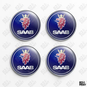 Könnte beinhalten: Vier runde Autoembleme mit dem SAAB-Logo. Jedes Emblem hat einen blauen Hintergrund und einen silbernen Rand. Das Logo zeigt einen roten Greif mit goldener Krone und das Wort "SAAB" in Silber.