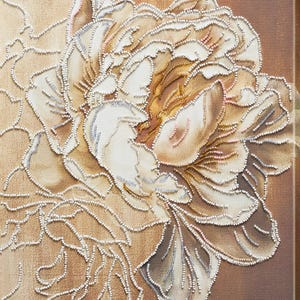 May include: A detailed artwork of a flower, with cream and tan petals and gold and pink accents. The flower is outlined with small, white beads, giving a textured appearance. The background is a warm brown. The artwork is a close-up of the flower.