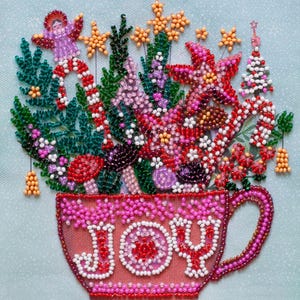 May include: A beaded Christmas-themed design featuring a pink teacup overflowing with festive elements. The cup is adorned with the word "JOY". The arrangement includes a candy cane, stars, a Christmas tree, and various flowers, all crafted from colorful beads. The background is a light blue.