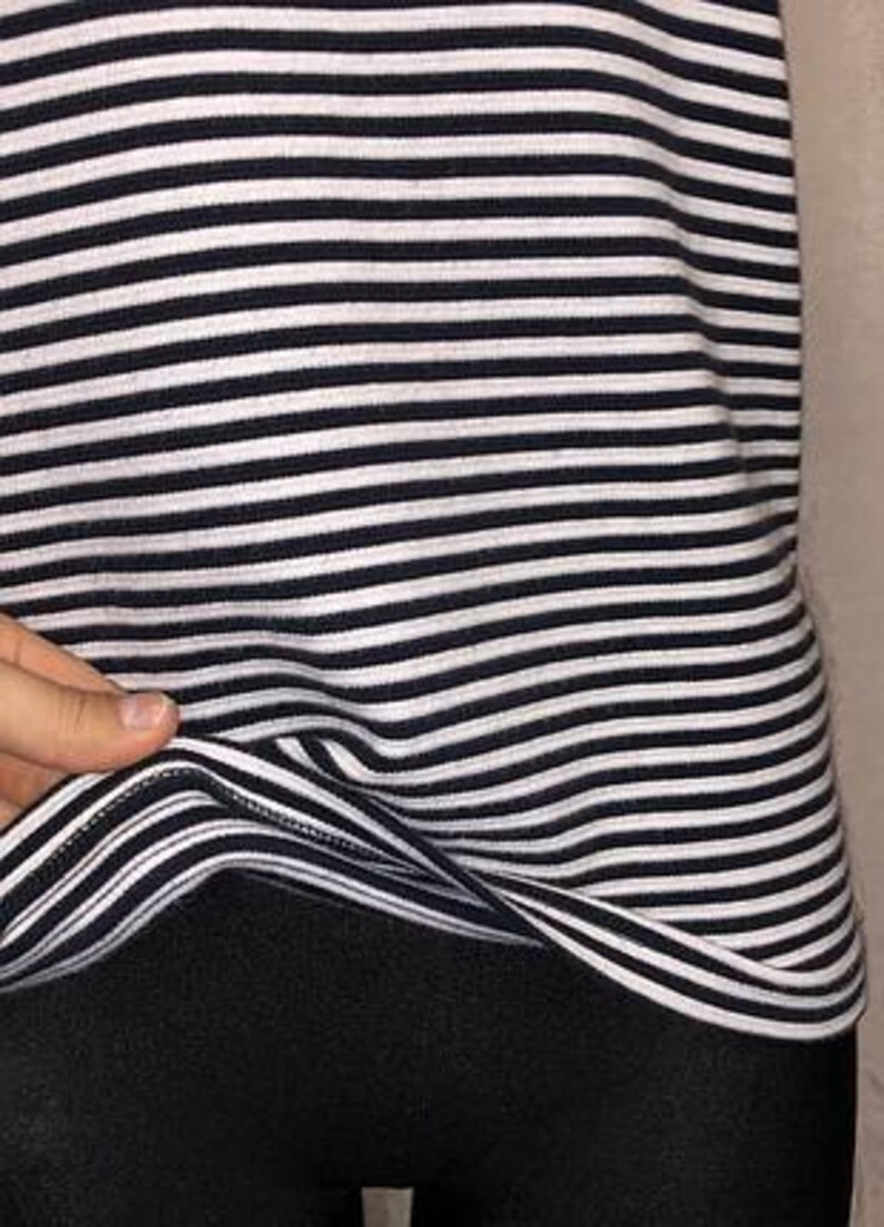May include: A black and white striped top. The top features horizontal stripes in a classic nautical style. The fabric appears to be a soft knit material. The bottom portion of the image shows black leggings or pants.