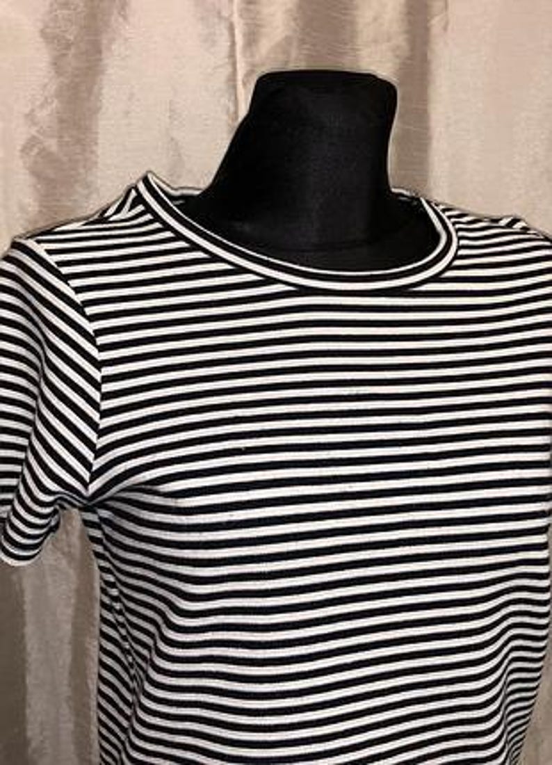 May include: A black and white striped t-shirt with a crew neck and short sleeves. The shirt is displayed on a black mannequin head. The stripes are horizontal and evenly spaced, creating a classic nautical look.