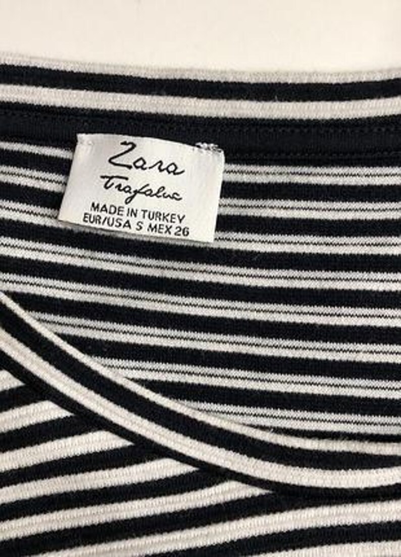 May include: Close-up of a black and white striped top. The top has a label that reads "Zara Trafaluc" and "Made in Turkey". The size is listed as EUR/USA S MEX 26. The fabric is a soft, knit material.