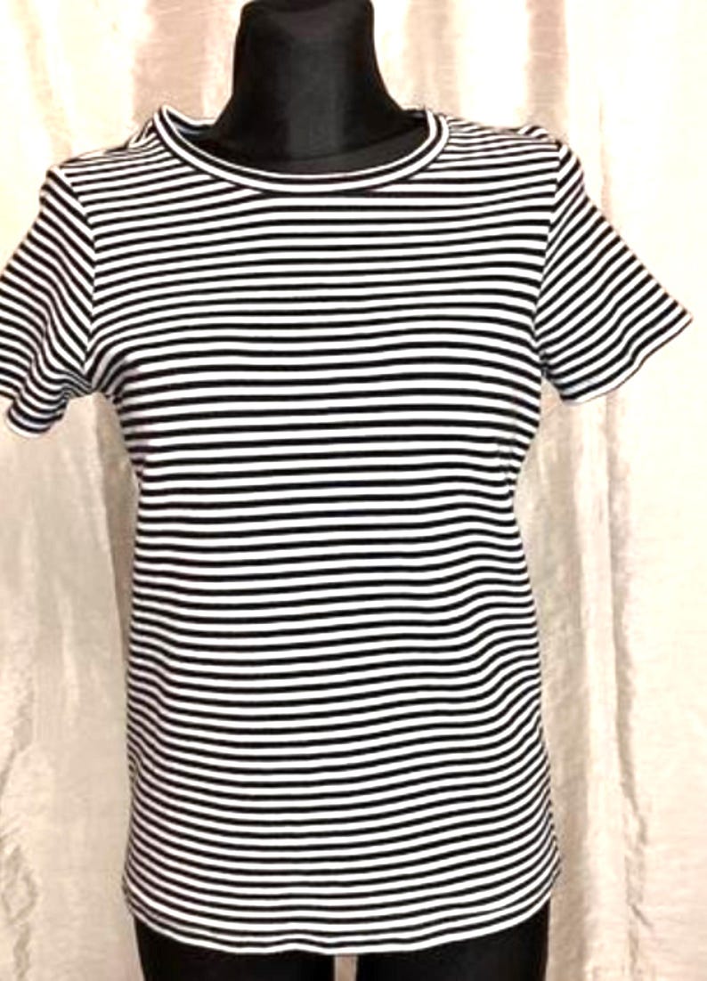 May include: A black and white striped t-shirt with short sleeves. The shirt is displayed on a black mannequin. The horizontal stripes are evenly spaced across the fabric. The neckline and sleeves are finished with a solid black trim.