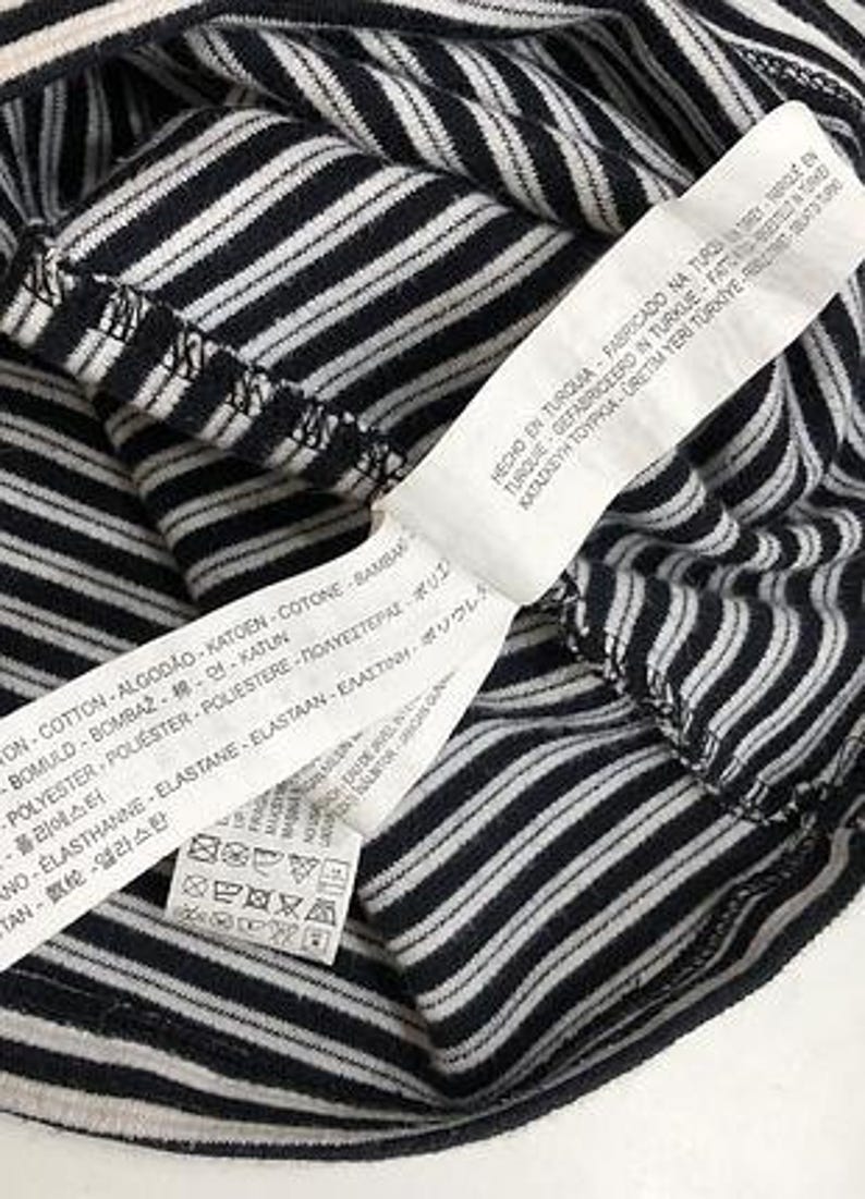 May include: Close-up of a black and white striped shirt. A white tag with text in multiple languages is attached to the shirt. The tag includes washing instructions and fabric composition.