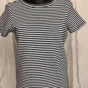 May include: A black and white striped t-shirt with short sleeves. The shirt has a round neckline and a classic horizontal stripe pattern. The garment is displayed on a black mannequin.