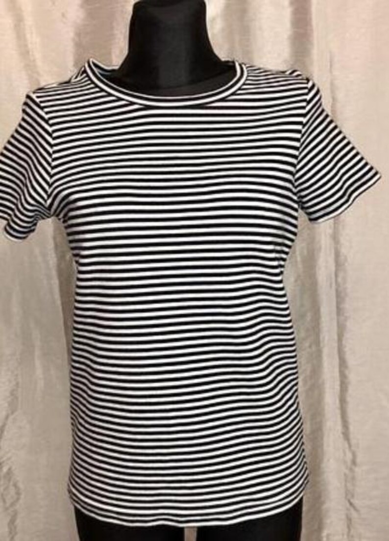 May include: A black and white striped t-shirt with short sleeves. The shirt has a round neckline and a classic horizontal stripe pattern. The garment is displayed on a black mannequin.