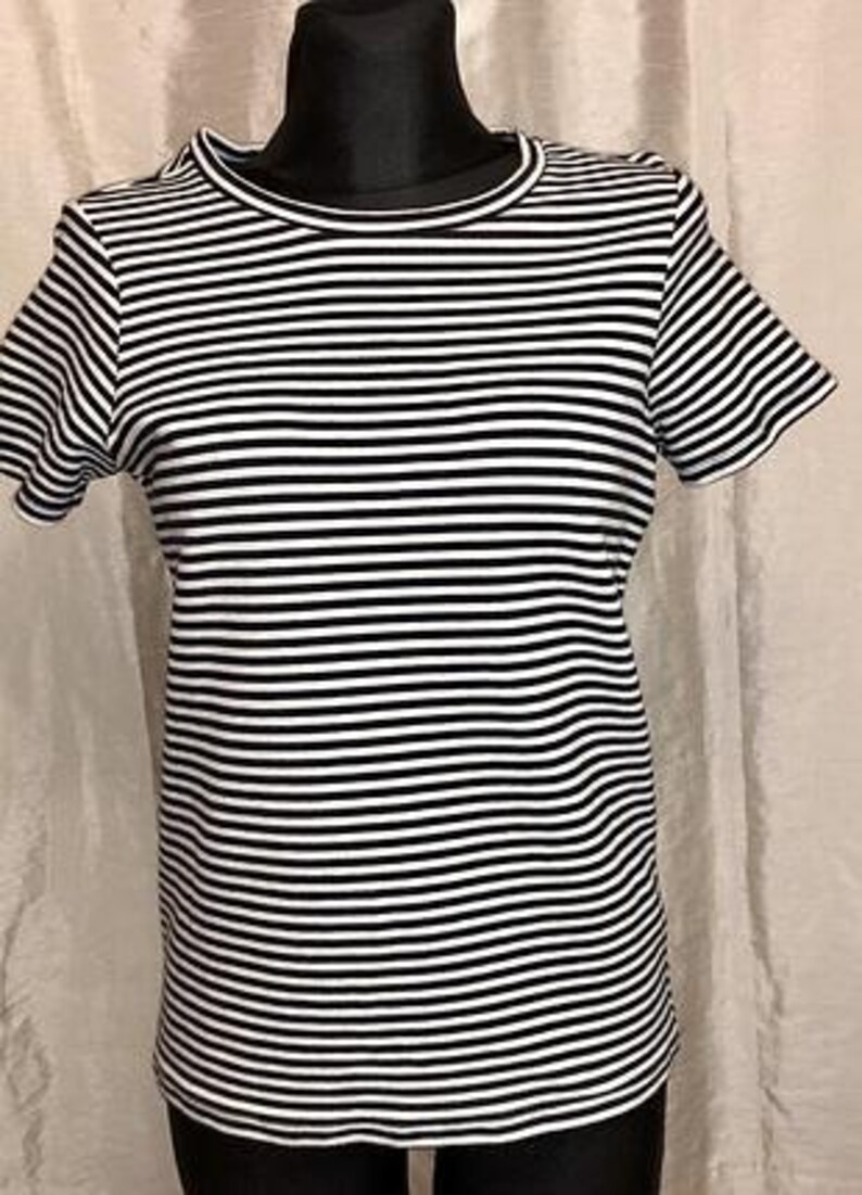May include: A black and white striped t-shirt with short sleeves. The shirt is displayed on a black mannequin. The stripes are horizontal and evenly spaced. The neckline and sleeves have a simple, clean finish.
