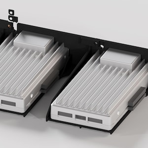 Puede incluir: Dos dispositivos electrónicos plateados y blancos con superficies acanaladas están montados en un bastidor negro. Los dispositivos tienen formas rectangulares con una pequeña parte superior cuadrada y tres aberturas rectangulares en la parte delantera.