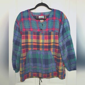 May include: A long-sleeved, multi-colored plaid shirt with a front pocket and drawstring hem. The shirt features a button-down neckline and a mix of blue, green, red, orange, and yellow plaid patterns. The shirt is hanging on a black hanger.