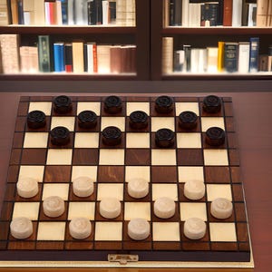 Op de afbeelding: Een houten dambord met zwarte en witte damstenen. Het bord is gemaakt van donkerbruin hout met lichtbruine en beige vierkanten. De zwarte stenen staan ​​aan de ene kant en de witte aan de andere kant. Het spel is klaar om te spelen.