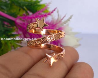 Könnte beinhalten: Ein roségoldfarbener Spiralring mit einem polierten Stern an jedem Ende. Das Band ist über die gesamte Länge mit einem geprägten Blumenmuster versehen. Das Metall hat eine reflektierende Oberfläche und das Design windet sich spiralförmig.