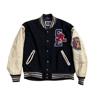 May include: A vintage black varsity jacket with cream-colored leather sleeves. The jacket features the letters "CR" in red and blue on the chest and a patch on the right sleeve. Ribbed cuffs and hem with white stripes complete the classic look.
