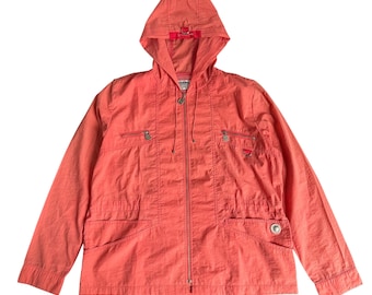 May include: Coral-colored hooded jacket with a full-length zipper, two front pockets, and two chest pockets. The jacket has a drawstring hood and a small logo on the chest. The jacket is made of a lightweight material.