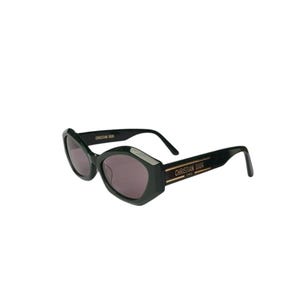 May include: Dark green sunglasses with a unique geometric frame shape. The lenses are a muted purple color. The right temple arm features the text "CHRISTIAN DIOR PARIS" in gold lettering.