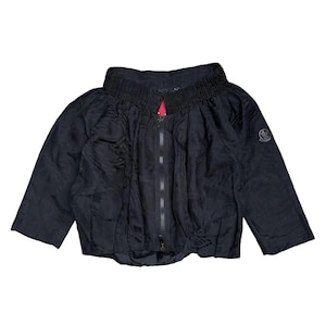 Puede incluir: Chaqueta negra con cuello alto fruncido y cremallera completa. La chaqueta tiene mangas tres cuartos y un pequeño logotipo en la manga superior izquierda. El interior de la cremallera es rosa.