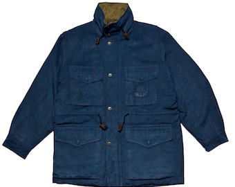 May include: A blue jacket with a high collar and multiple pockets. The jacket has a button-up front and drawstrings at the waist. The collar is lined with a contrasting brown fabric. The jacket has a logo on the chest.