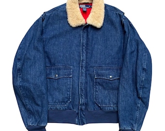 May include: A blue denim jacket with a tan faux fur collar and a red interior lining. The jacket has two front pockets and a navy blue ribbed hem and cuffs. A classic style.