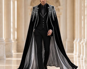 Puede incluir: Una capa larga de terciopelo negro con intrincados bordados plateados en los hombros, sobre un chaleco negro, camisa negra y pantalones negros. La capa tiene un forro plateado en contraste y ribetes blancos en los bordes delanteros.